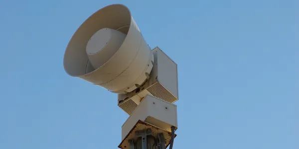 An outdoor warning siren mounted on a pole against a clear sky